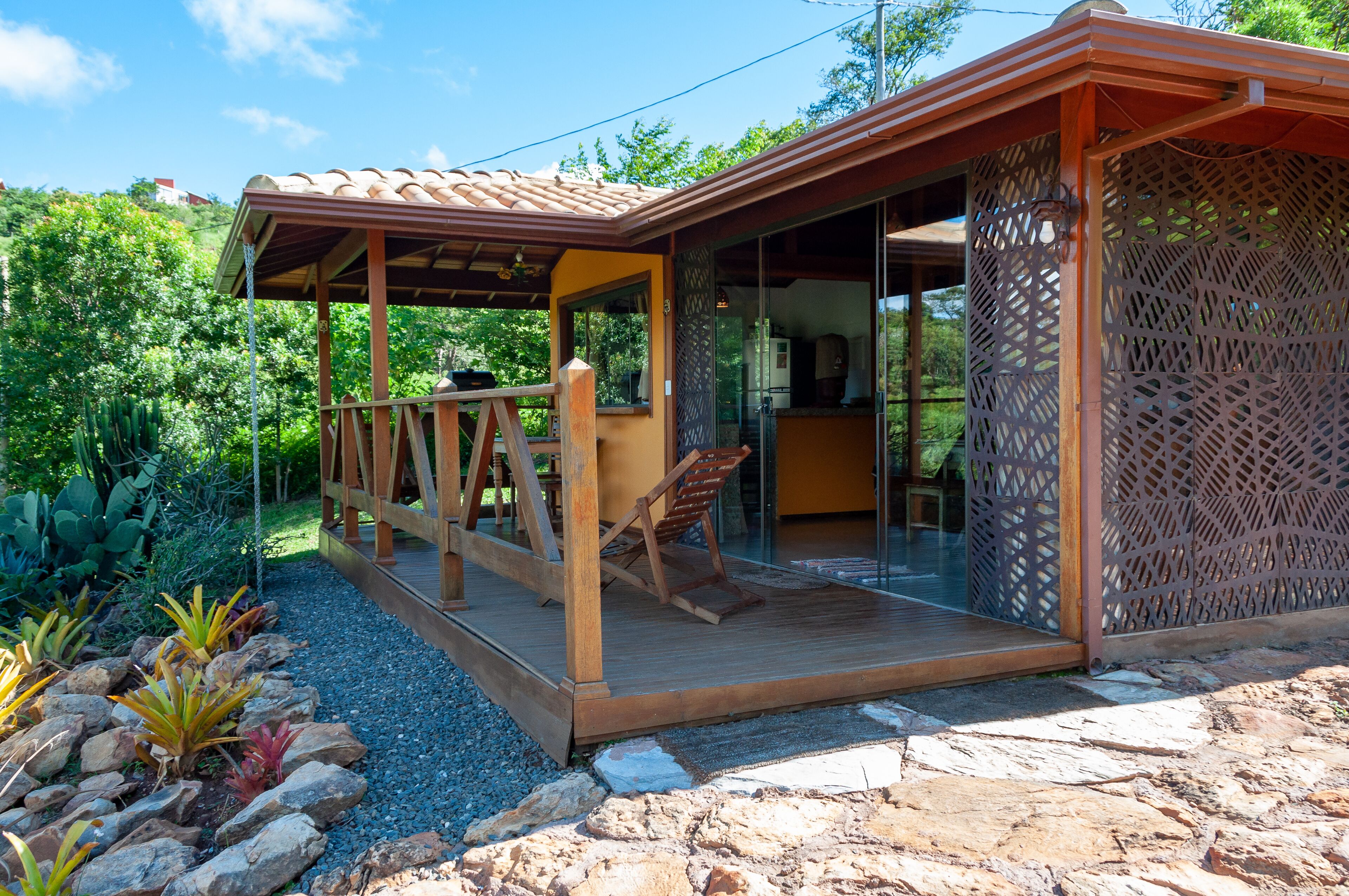 A wooden deck with a pergola, a glass door leading inside, and a patio area with a chair.