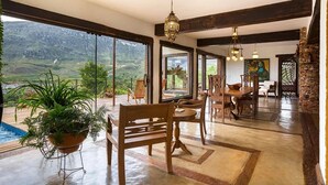 A spacious dining area with a view of a mountainous landscape through large windows, wooden furniture, and a hanging light fixture. - Sitio Jatoba Lapinha da Serra (Santana do Riacho)