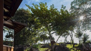 A wooden deck with a view of a landscaped garden, including rocks, grass, and trees. - Sitio Jatoba Lapinha da Serra (Santana do Riacho)