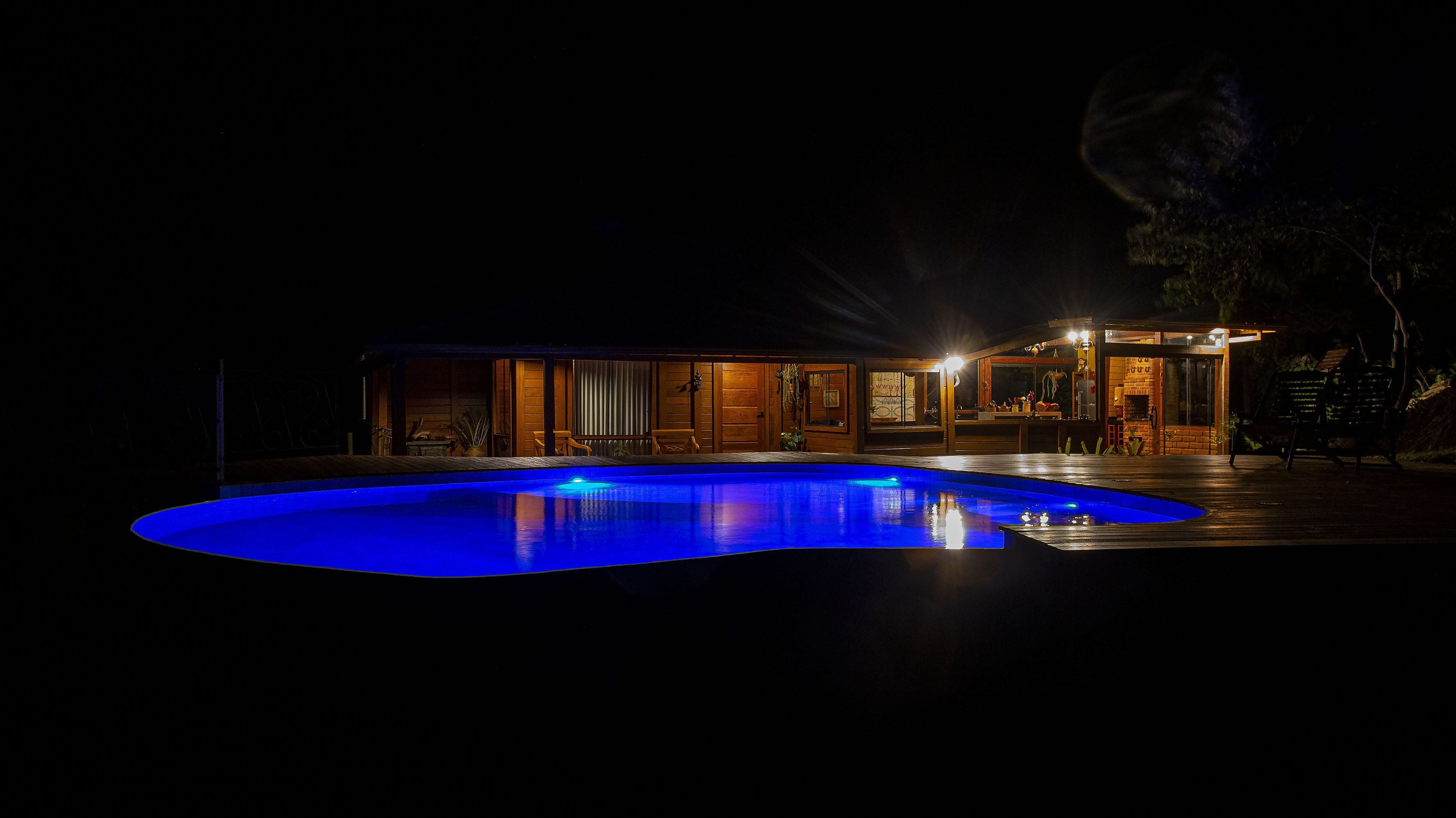 Vista nocturna de una casa con piscina, fachada de madera y entrada bien iluminada.