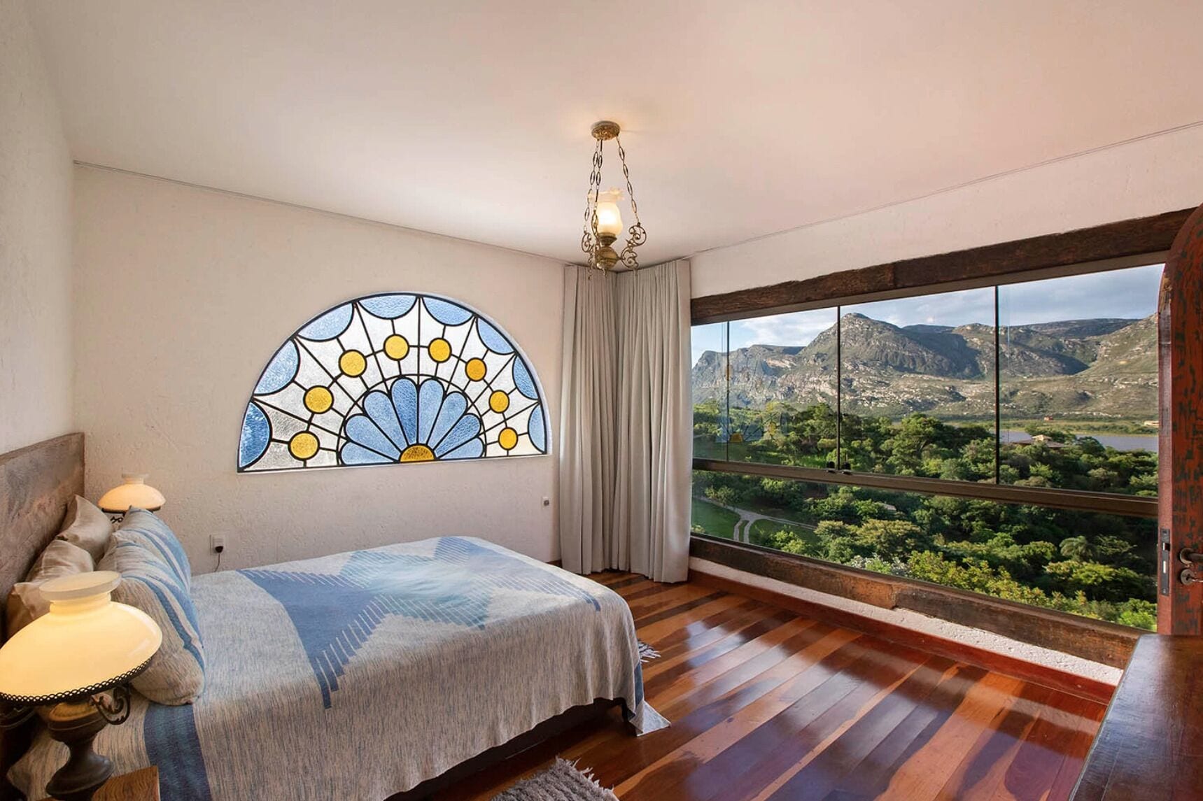 Een slaapkamer met een groot raam, een bed, een kroonluchter en een glas-in-loodraam.