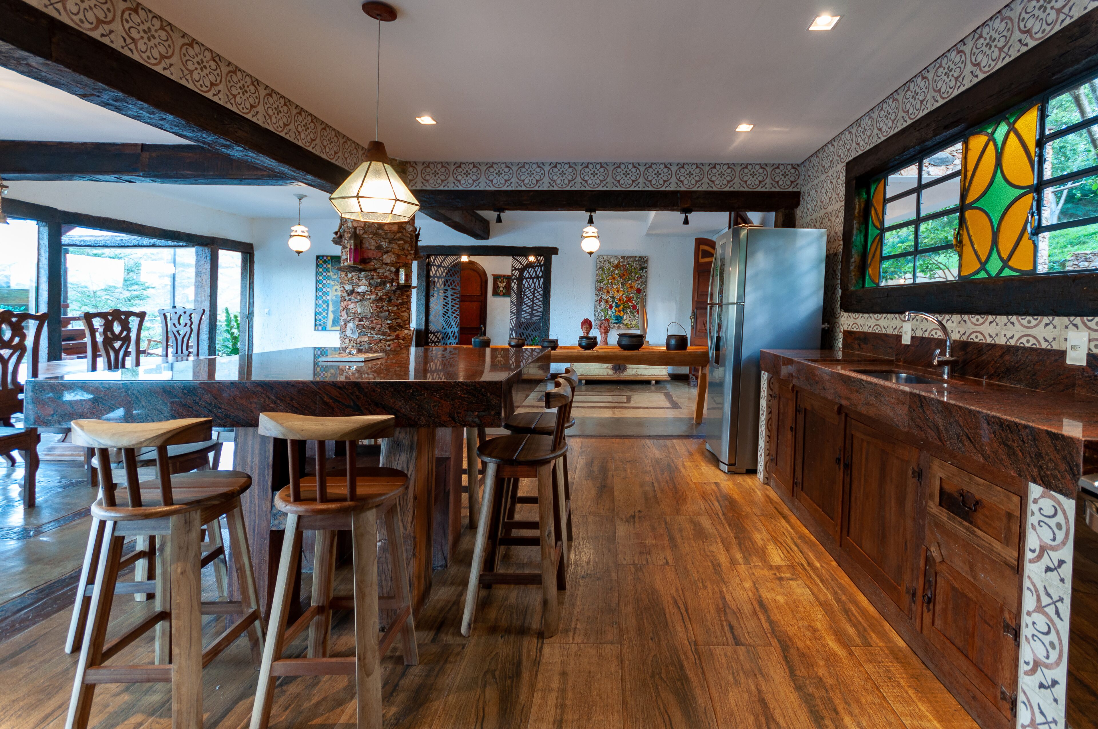 A spacious kitchen with wooden bar stools, a large island, and a view through a window.