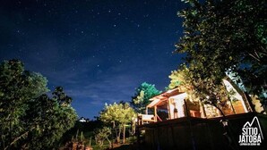 A night sky with stars, a building with a wooden structure, and trees. - Sitio Jatoba Lapinha da Serra (Santana do Riacho)