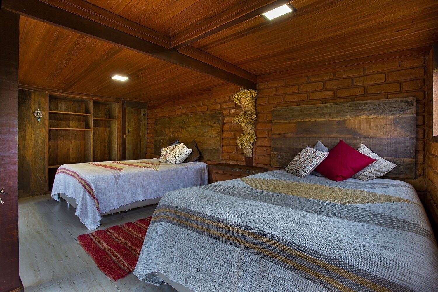 A cozy room with two beds, wooden walls, and a brick fireplace.
