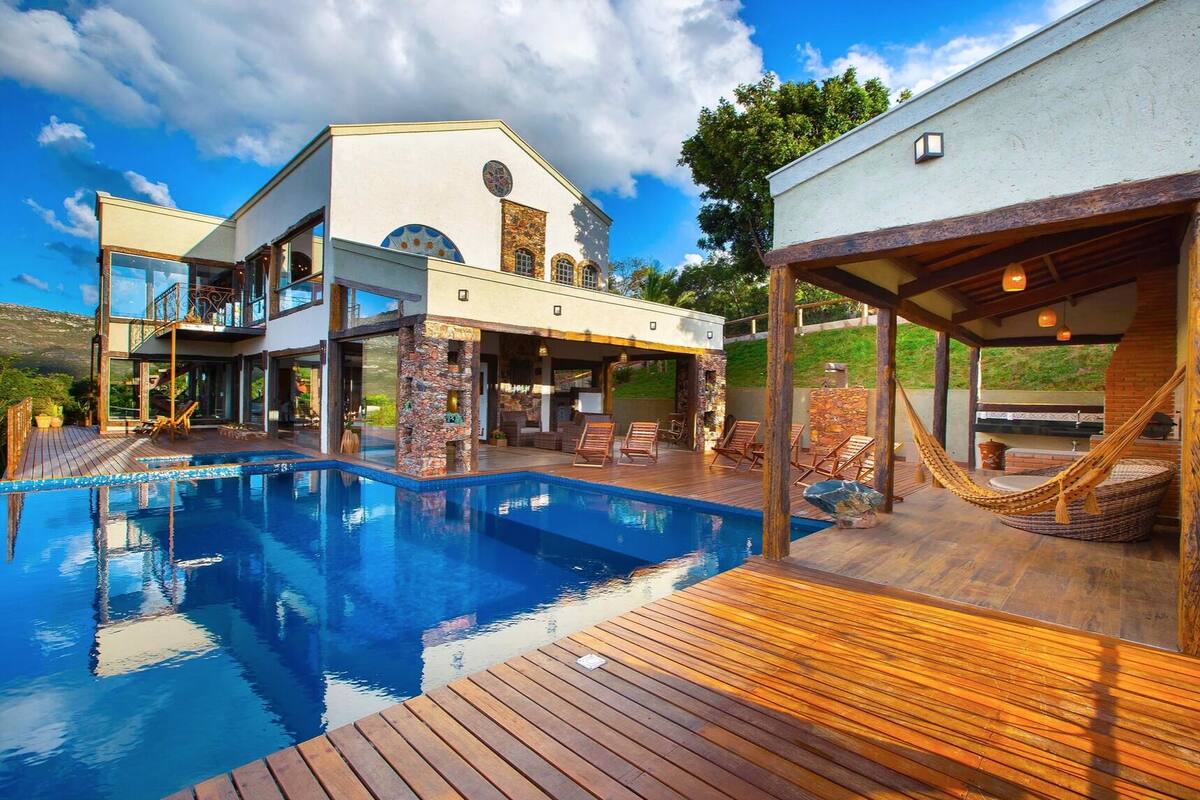 Une maison moderne dotée d’une grande piscine, d’un espace salon extérieur et d’un pilier en pierre.