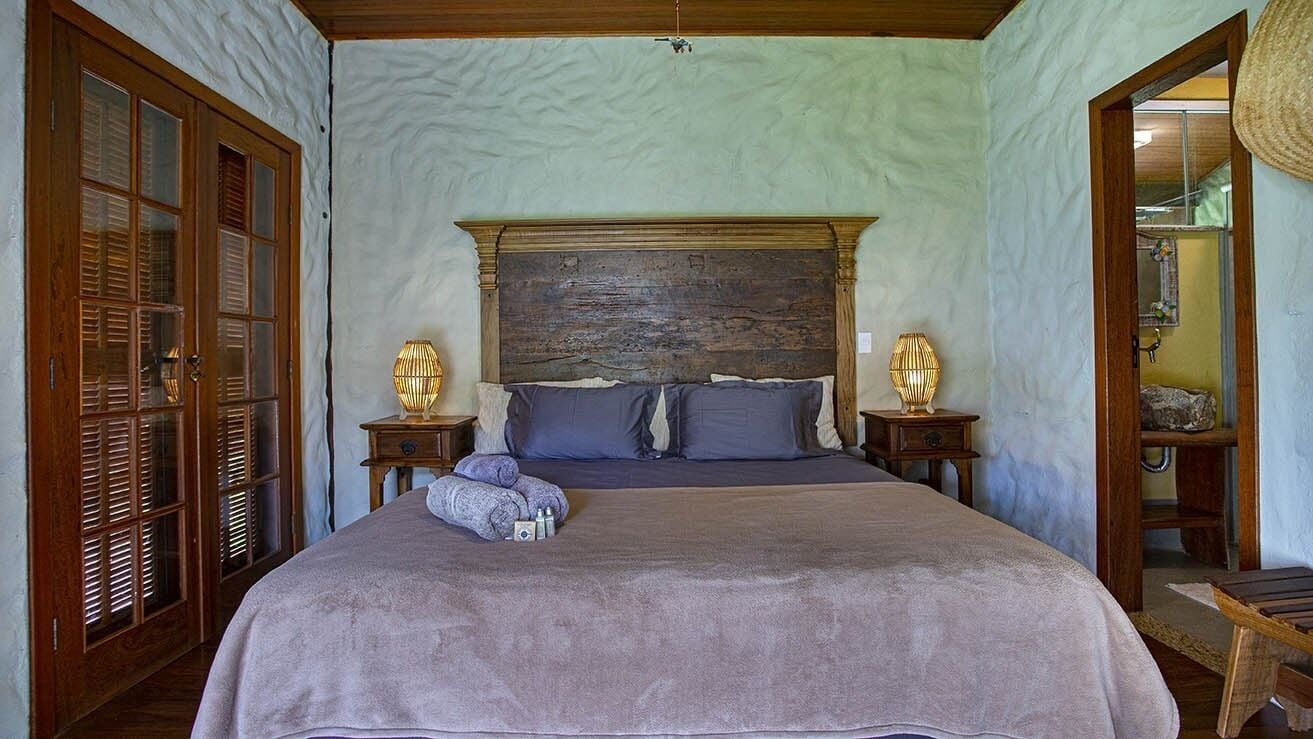A bedroom with a large bed, wooden headboard, two bedside tables with lamps, and a door with glass panels.