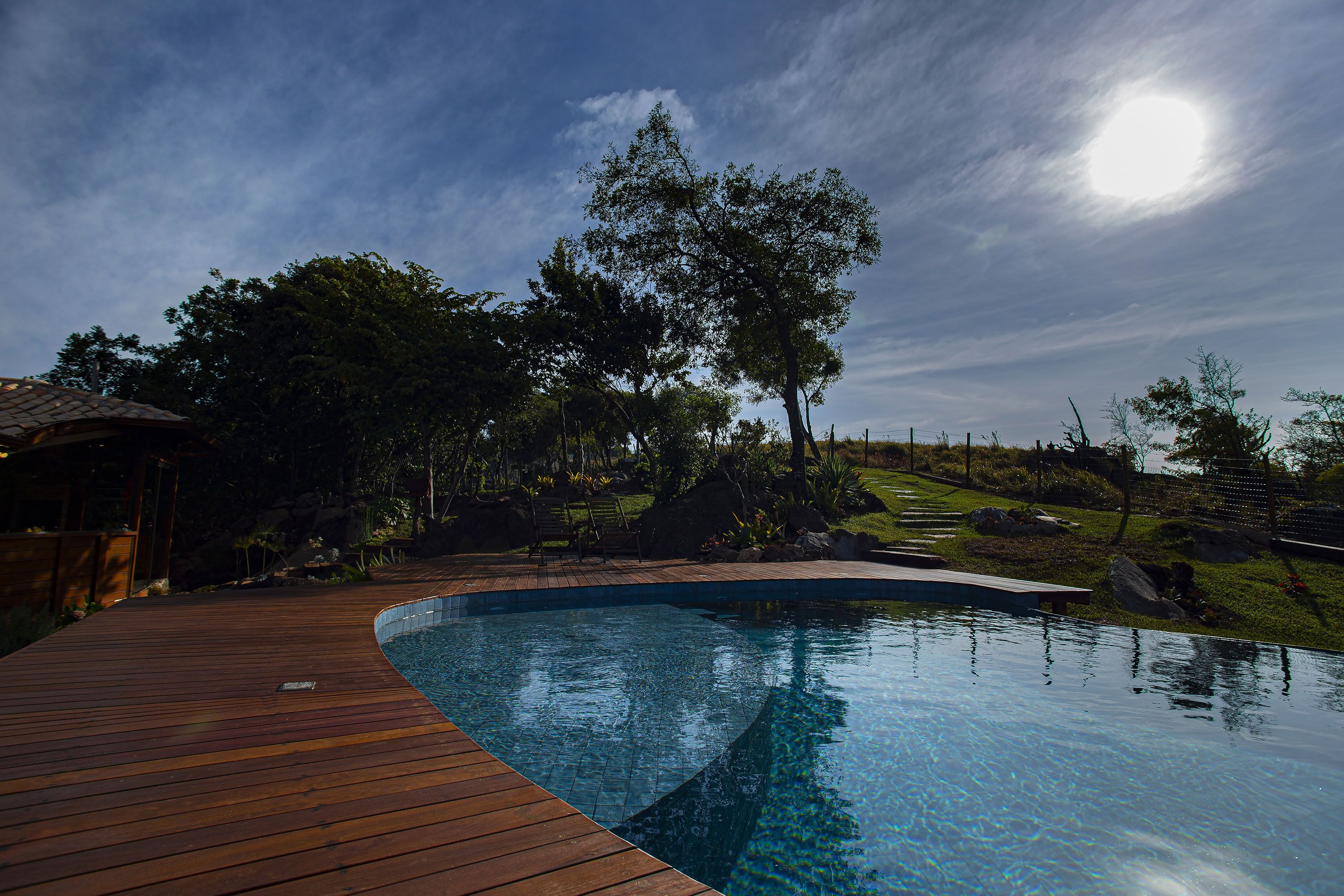 Piscina com deck de madeira, rodeada por árvores e paisagem gramada.