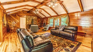 Ein rustikales Holzhaus-Interieur mit Holzbalkendecke, Ledersofas, einem Kamin aus Stein und einem großen Fenster.