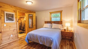 Ein schlicht eingerichtetes Schlafzimmer im Blockhausstil mit Bett, Nachttisch und Fenster.