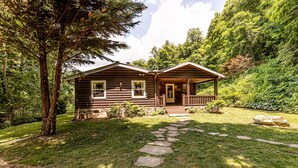 Eine Blockhütte mit Veranda, umgeben von einem Kiesweg und üppiger Bepflanzung.
