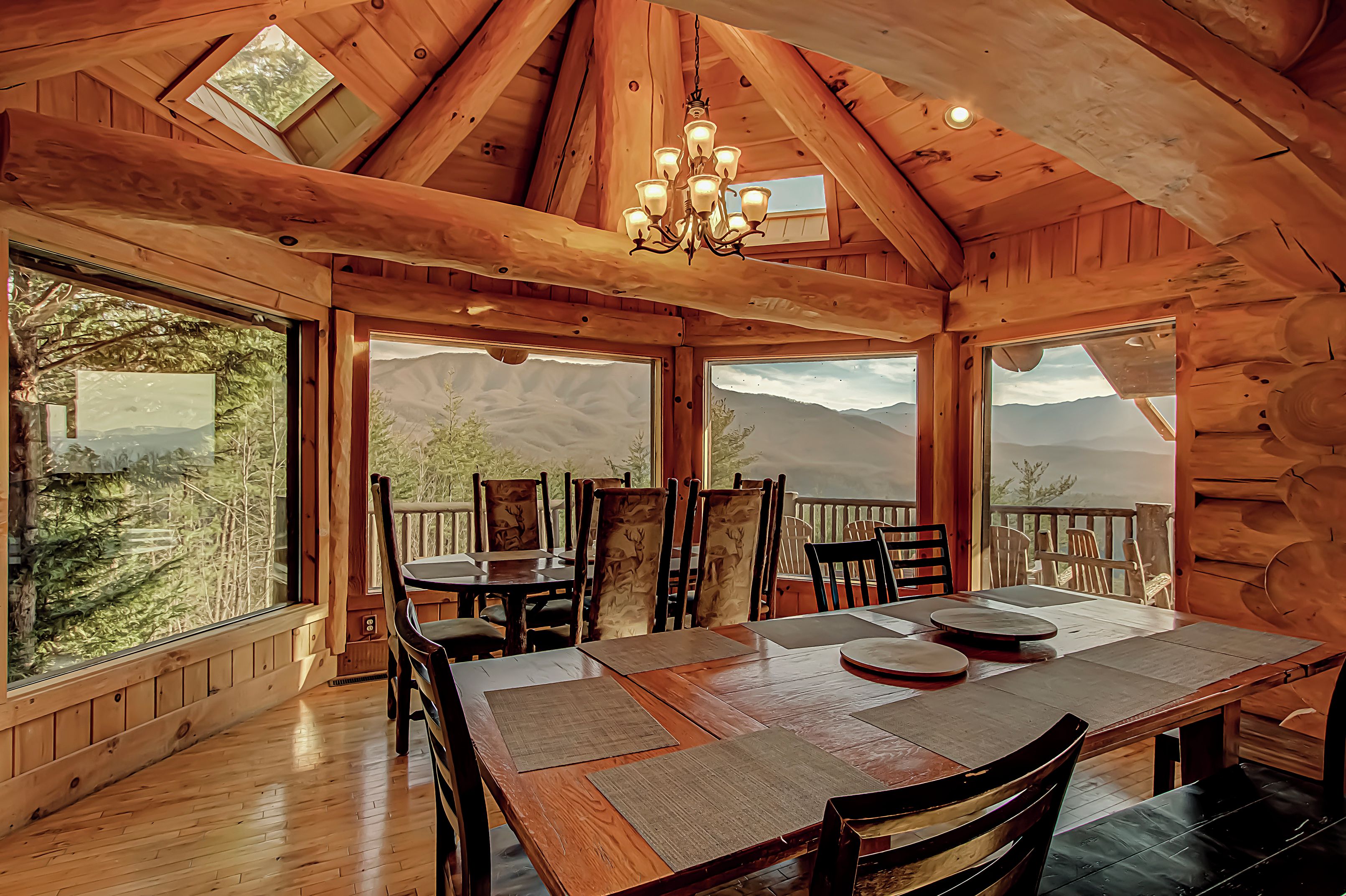A wooden dining area with a high ceiling, large windows, and a chandelier.
