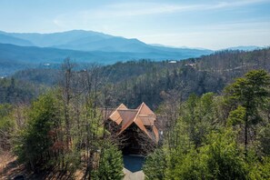 A cabin with a triangular roof nestled in a forest, surrounded by mountains.