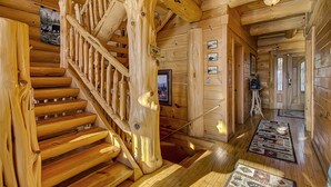 A wooden staircase with a unique design, a hallway with framed pictures, and a patterned rug on the floor.