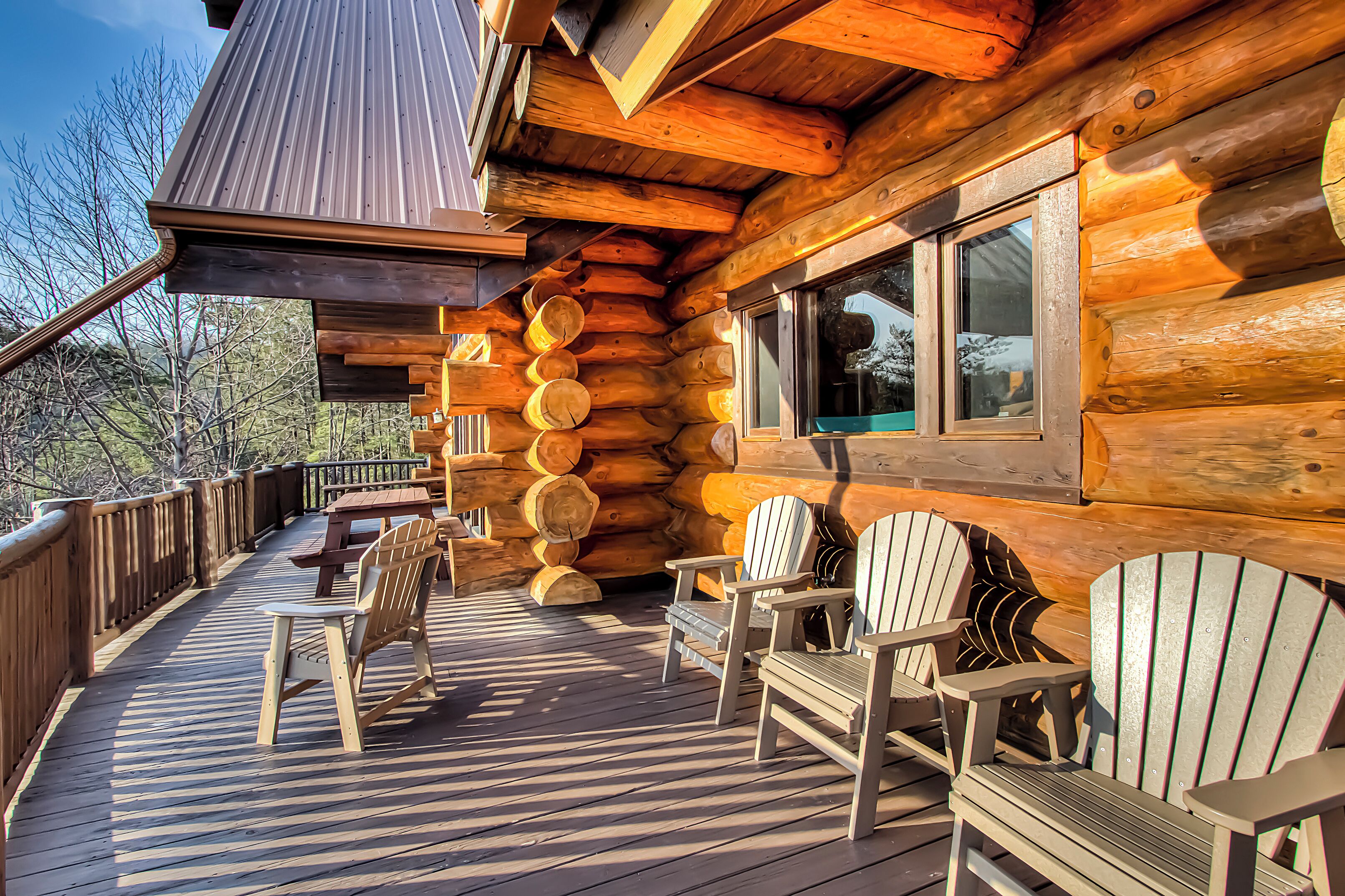 A log cabin with a wooden deck, several Adirondack chairs, and a large window.