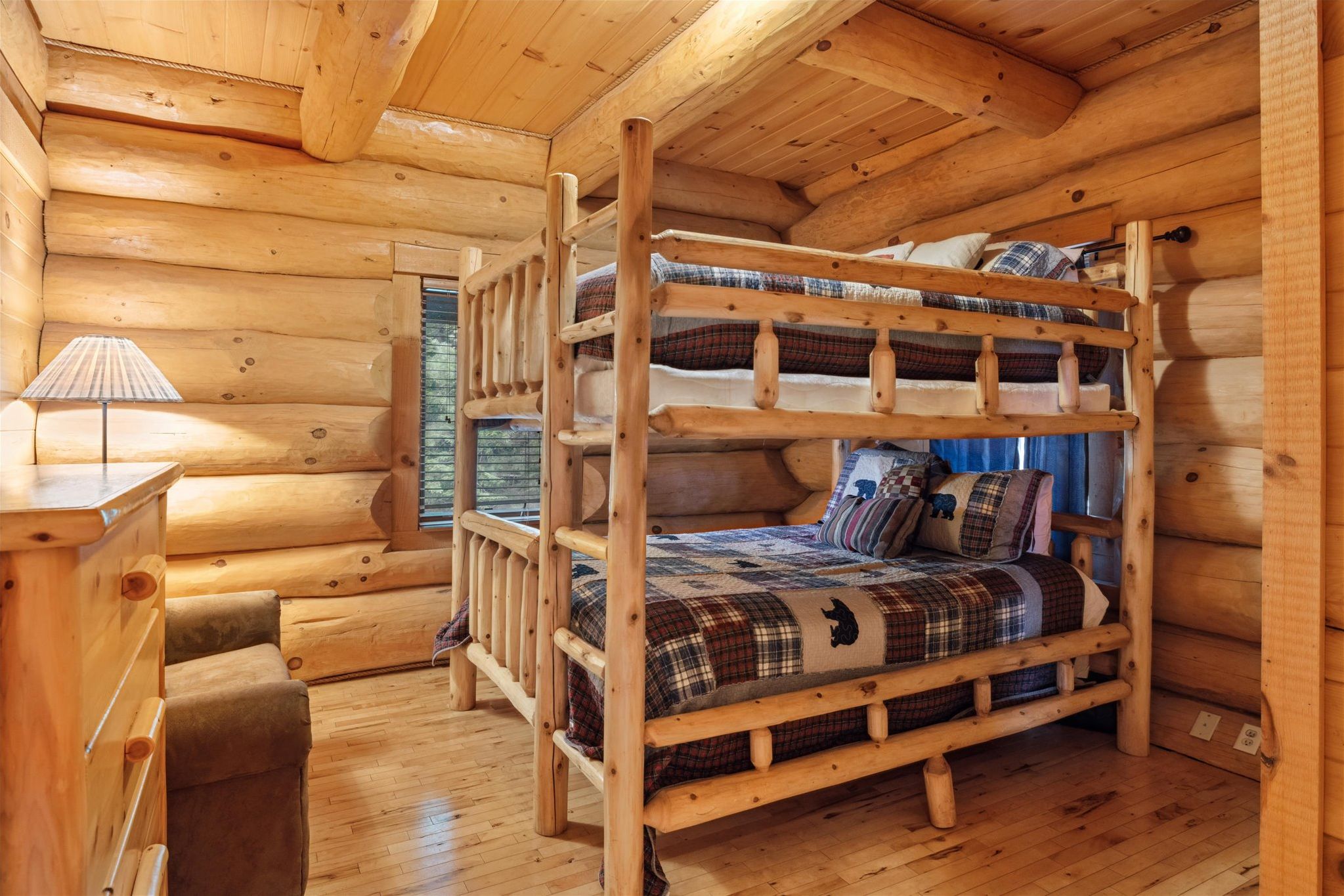 A wooden cabin interior with a bunk bed, a desk, and a lamp.