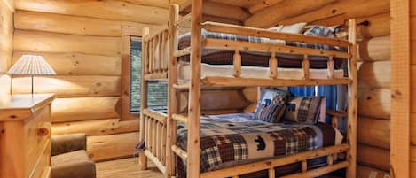 A wooden cabin interior with a bunk bed, a desk, and a lamp.
