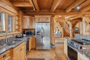 A log cabin kitchen with granite countertops, stainless steel appliances, and wooden cabinets.