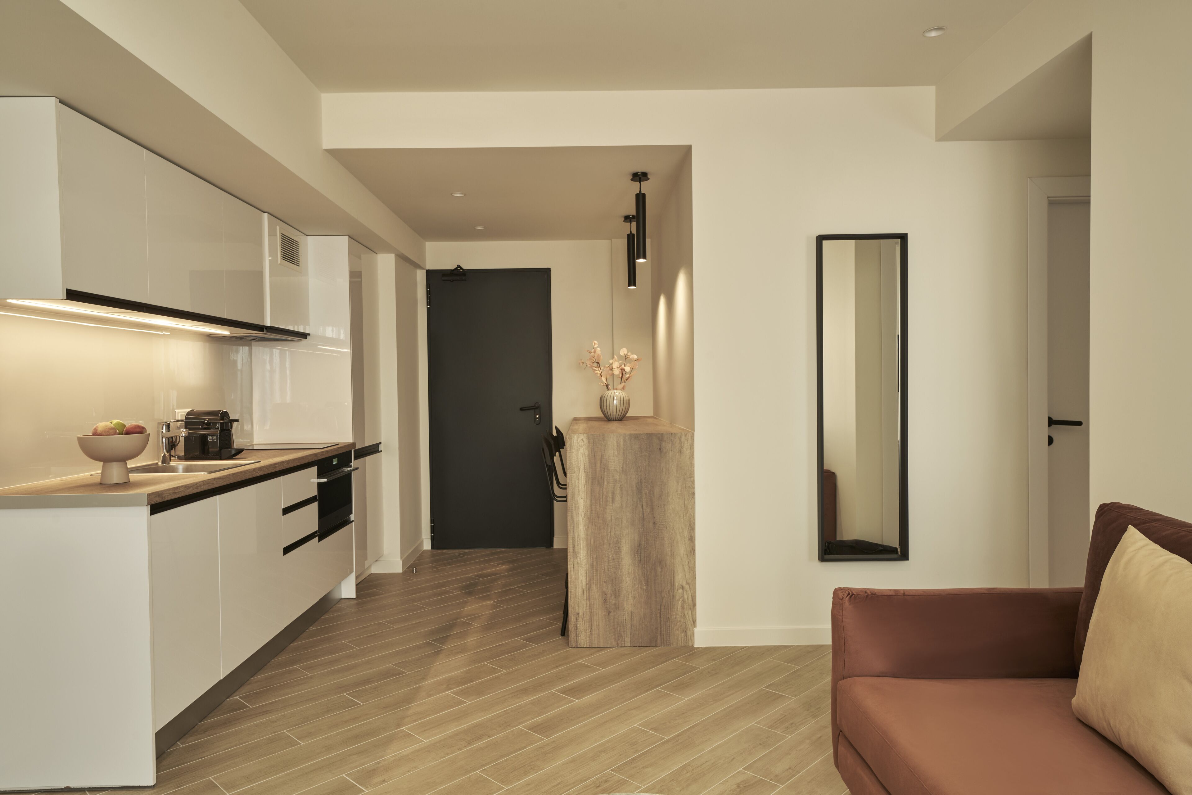 A modern kitchen with white cabinetry, a wooden island, and a brown leather sofa in a living area.