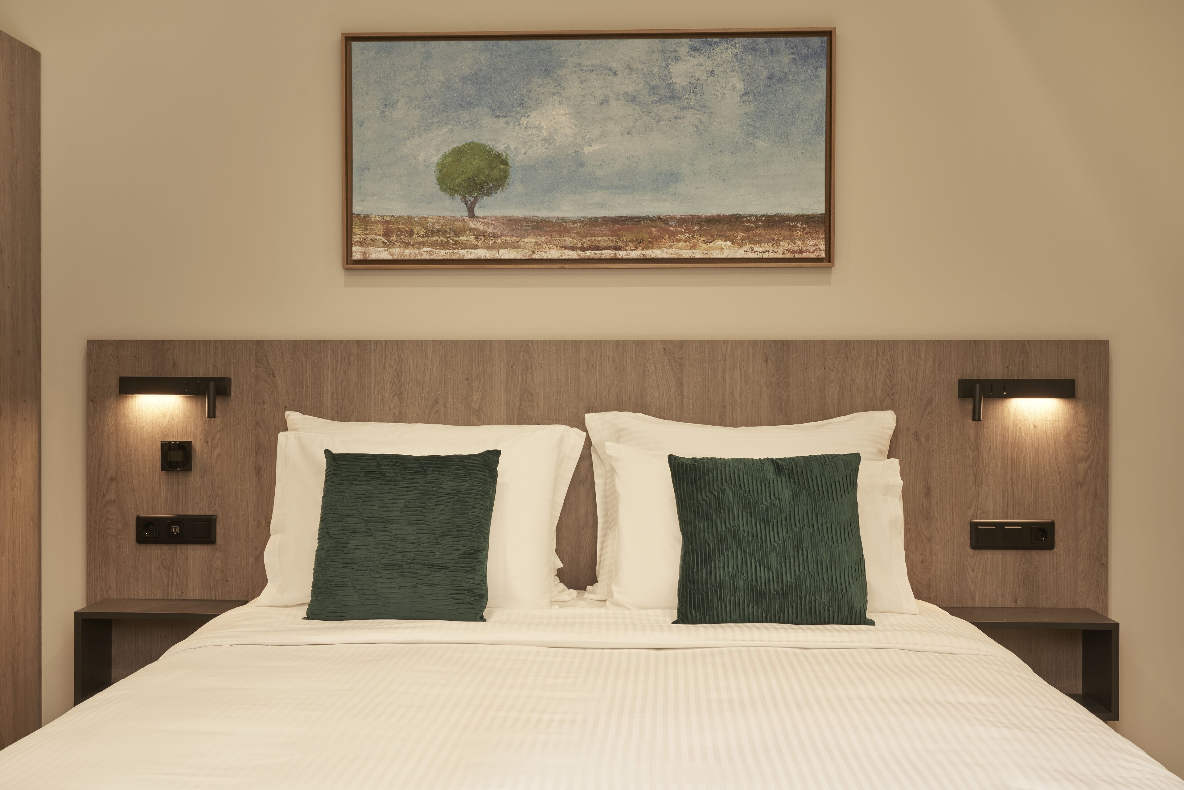 A neatly made bed with two pillows, a painting of a tree on the wall, and two bedside lamps.