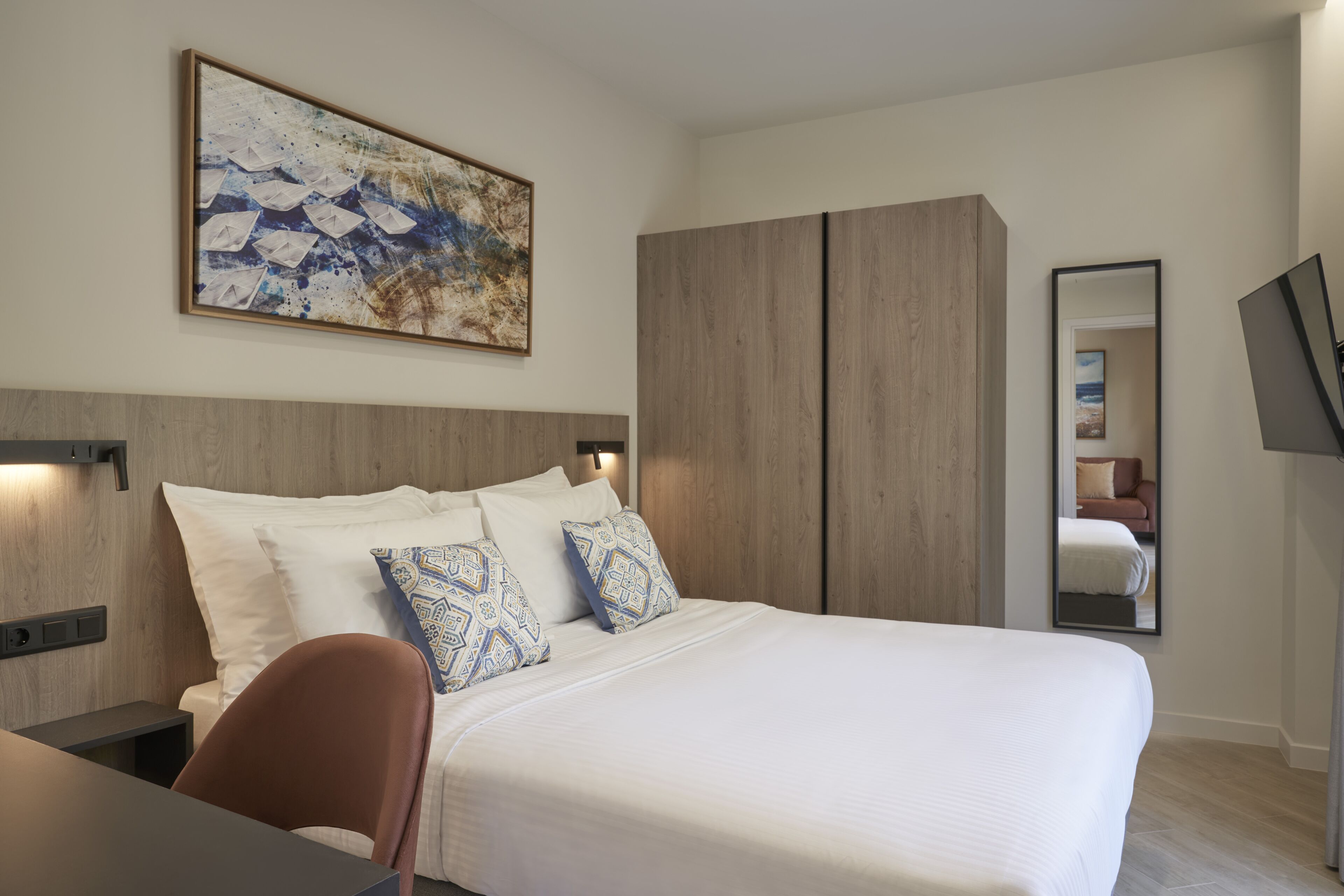 Een moderne hotelkamer met een groot bed, een bureau, een stoel, een kledingkast en een schilderij aan de muur.