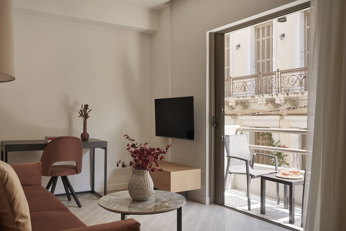 En moderne stue med sofa, spisebord, fjernsyn og en balkon med udendørs møbler.