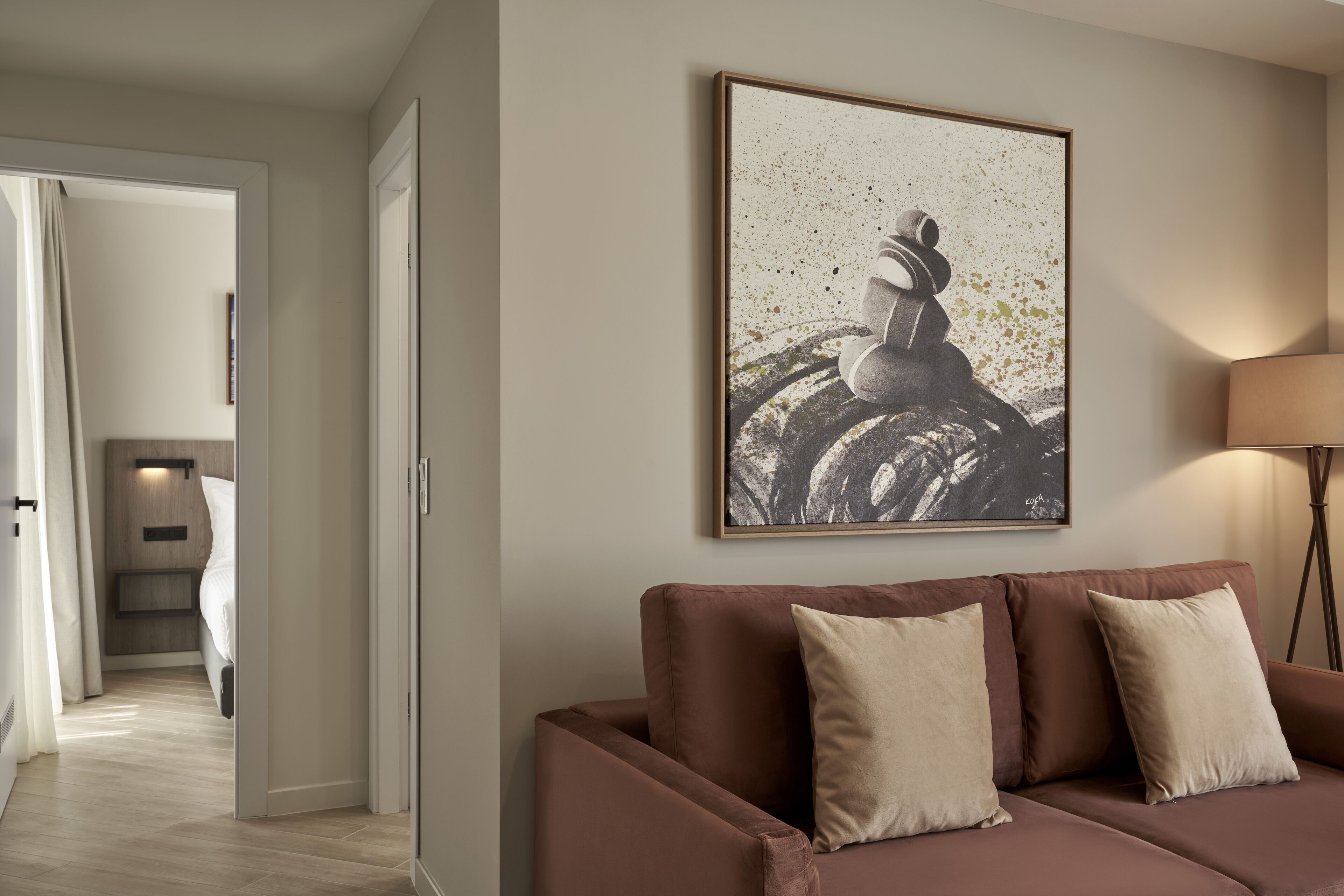 A modern living room with a brown sofa, a framed abstract painting, and a floor lamp.