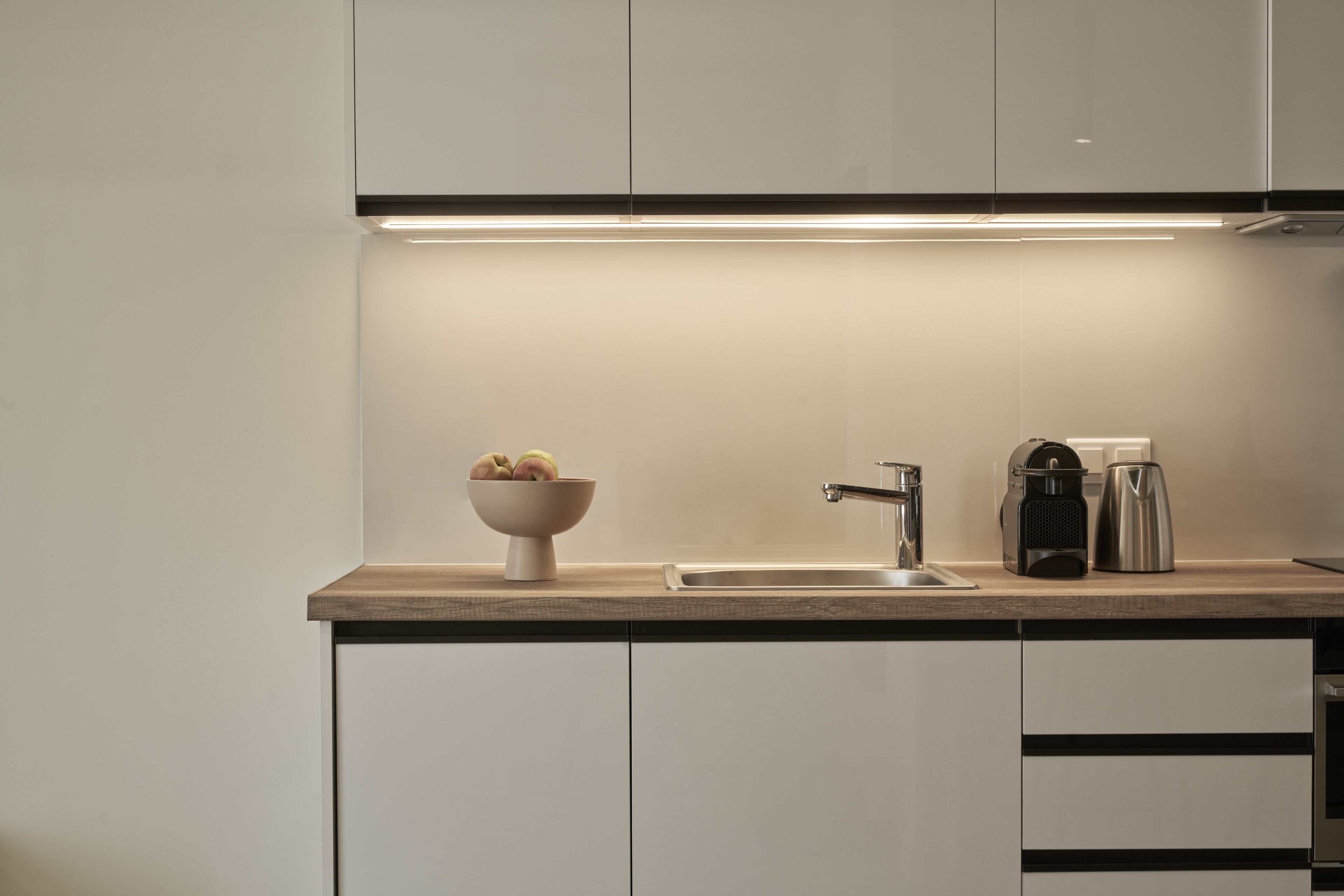 Una cocina moderna con una encimera, un lavamanos, una cafetera y un bol con fruta.