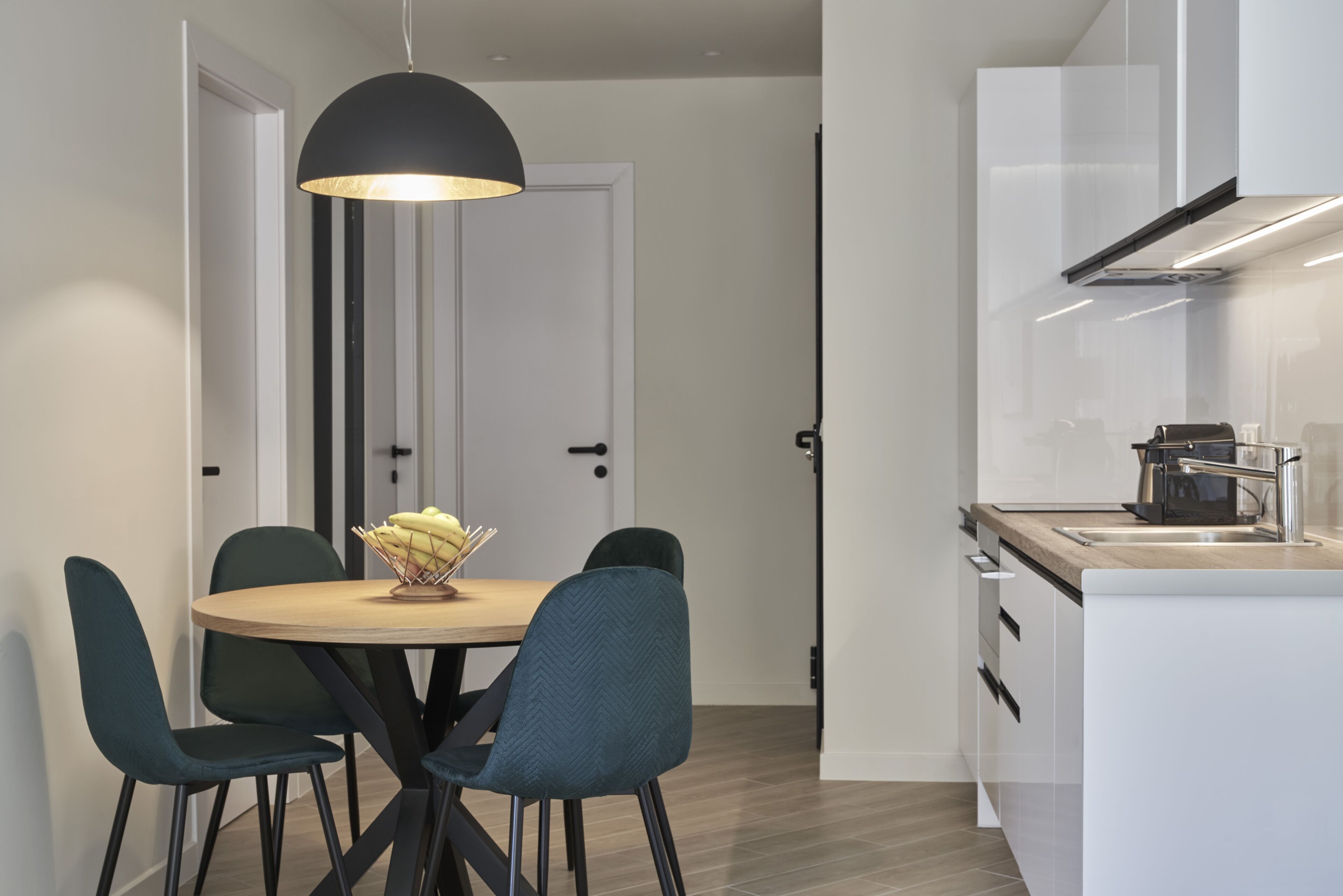 A modern kitchen with white cabinetry, a wooden countertop, and a black pendant light above the dining table.