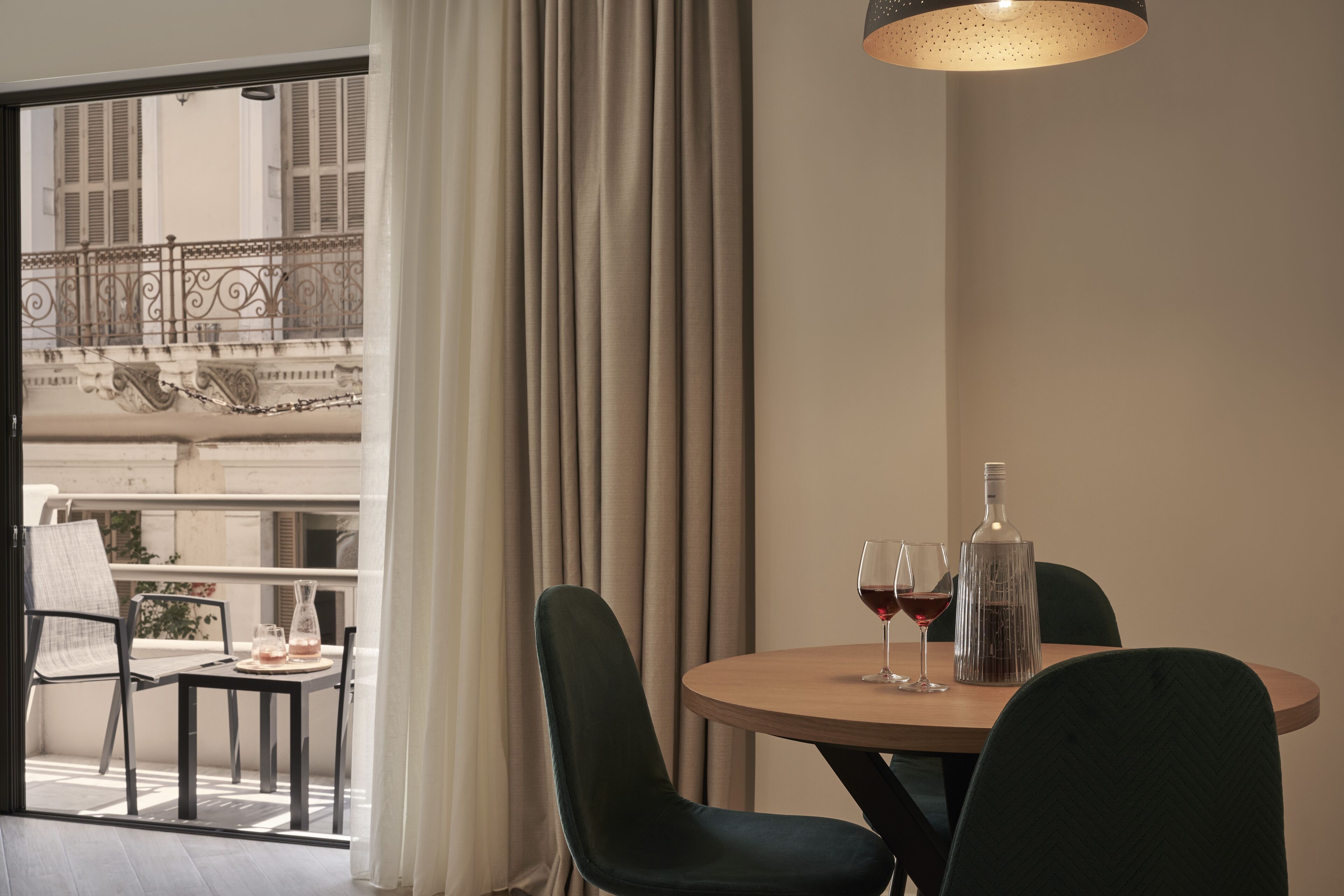 Un coin repas avec une table ronde, deux chaises, une bouteille et deux verres de vin rouge.