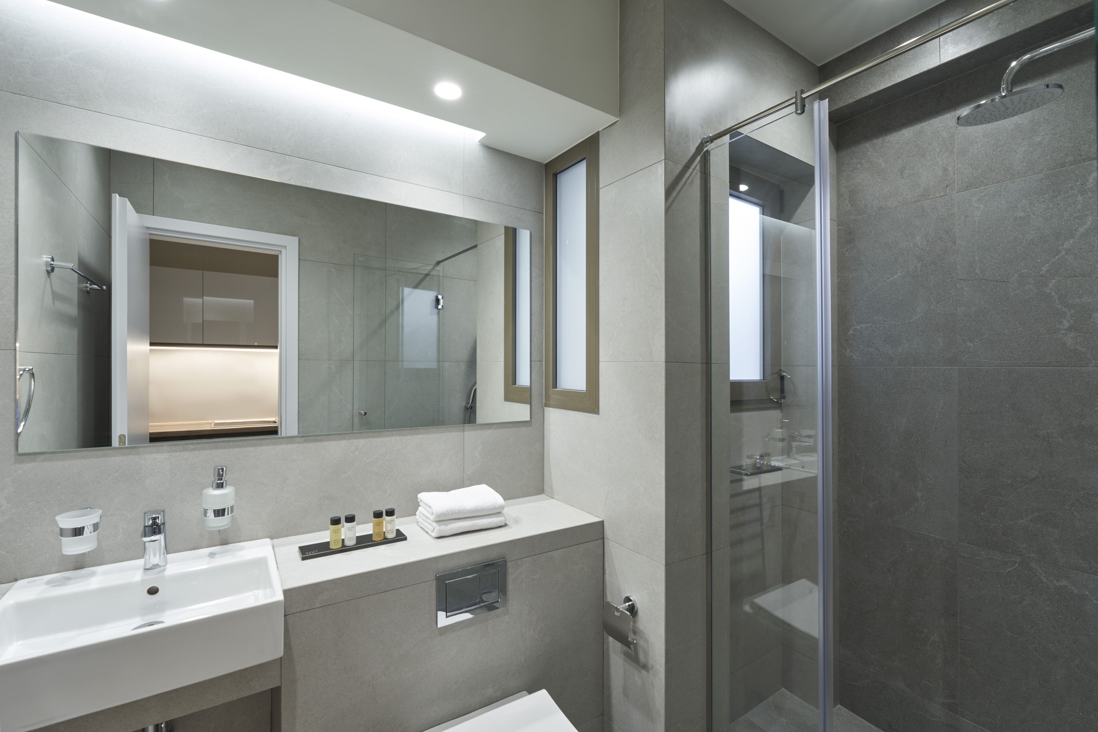 Une salle de bain moderne avec un grand miroir, deux lavabos, une douche et un espace douche fermé par des parois de verre.