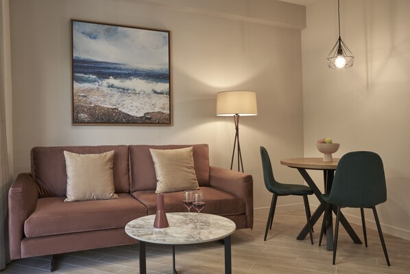 A living room with a brown sofa, a round coffee table, two wine glasses, a lamp, and a painting of a beach scene.