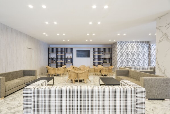 A modern lounge area with sofas, wicker chairs, and a patterned ottoman. - Hotel Best Punta Dorada (Salou)