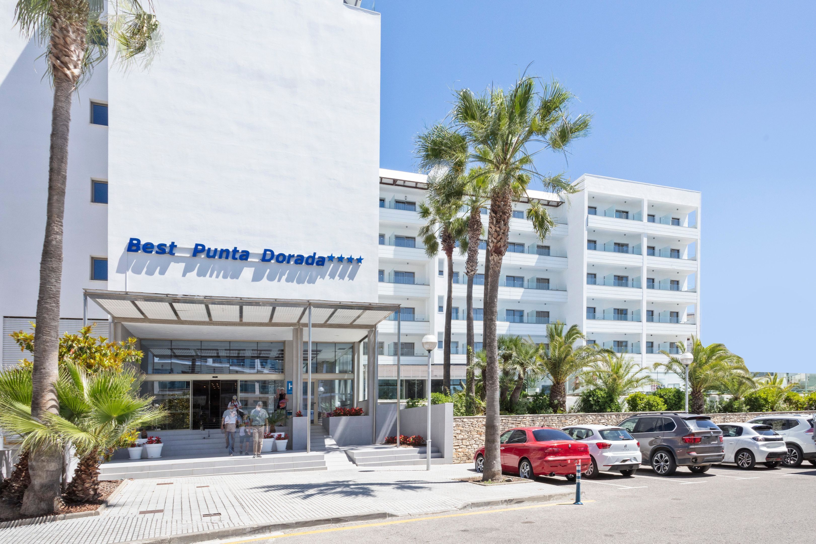 Et moderne hotel med tydelig indgang, palmer og parkeringsplads.