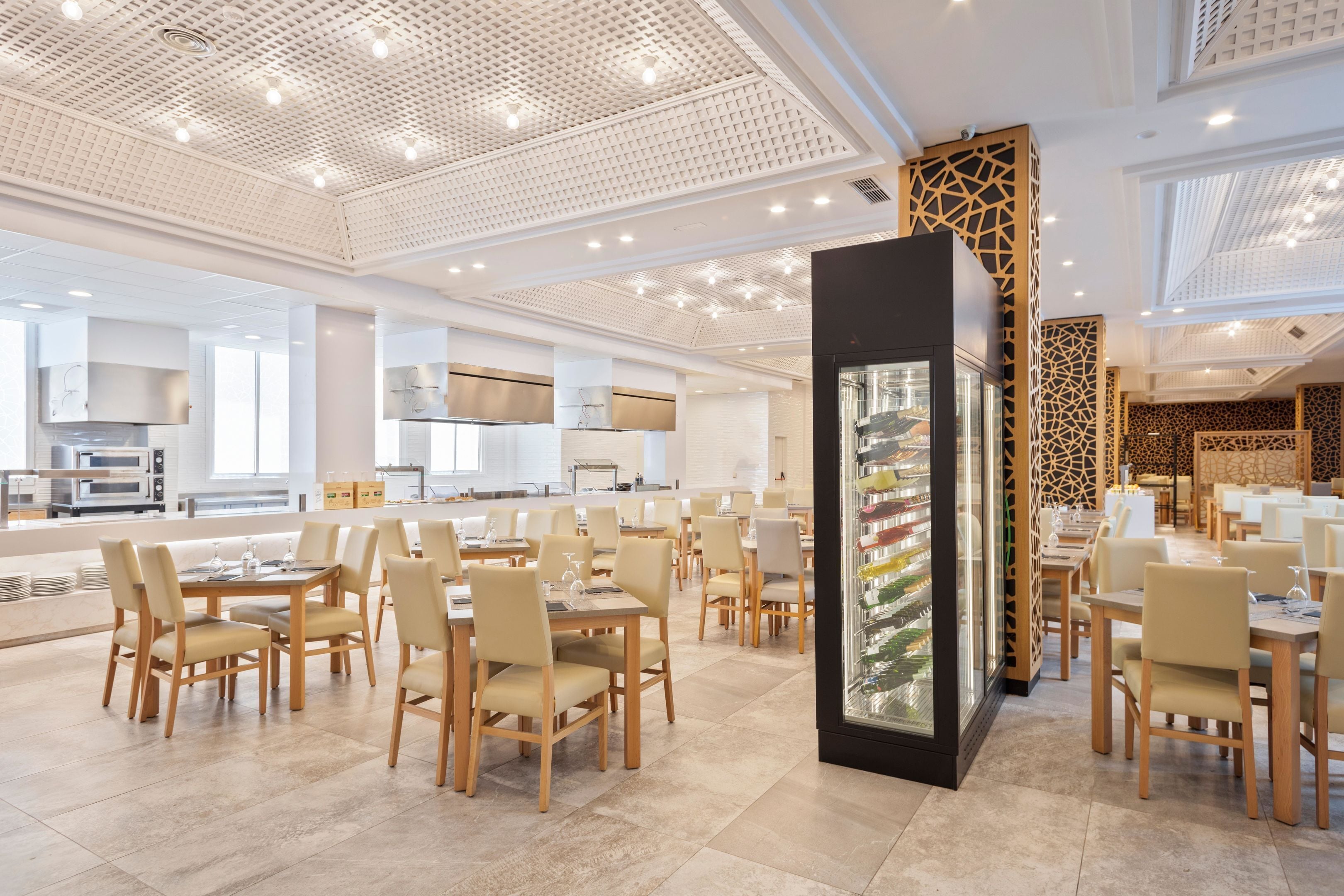 Un comedor amplio con varias mesas y sillas, un expositor de vidrio decorativo en el centro, y un diseño moderno del techo.