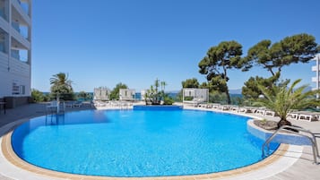 Una piscina grande y cristalina de color azul con sillones de descanso y vistas al mar.