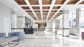 Un vestíbulo moderno con suelo de mármol, un mostrador de recepción, zonas de estar y vistas al exterior.