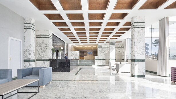 Eine moderne Lobby mit Marmorboden, einer Rezeption, Sitzbereichen und Blick ins Freie.