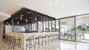 Zona de bar moderna con encimera de mármol, taburetes, iluminación colgante y amplias ventanas con vistas al exterior.