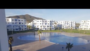 Zona de piscina con barandilla azul, rodeada de edificios blancos y una palmera.