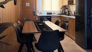 Una cocina moderna con armarios de madera, un refrigerador negro, una mesa de comedor con sillas y una lámpara colgante original.