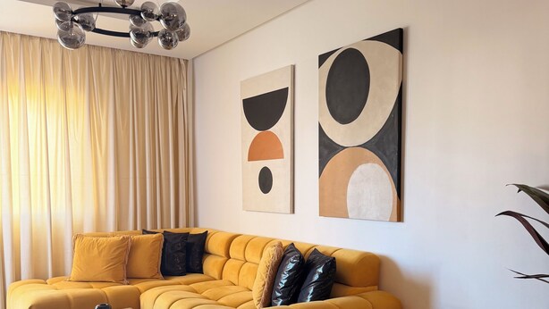 Una sala de estar moderna con un sofá seccional, una mesa de centro, arte abstracto en la pared y un tapete estampado.