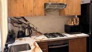 Una cocina moderna con armarios de madera, encimera de mármol, estufa a gas, refrigerador negro y microondas.
