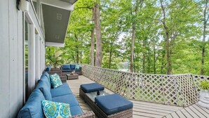 Eine überdachte Terrasse im Freien mit einer Couch und Kissen, umgeben von einem Gitterzaun und Bäumen.