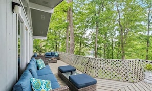 A covered outdoor deck with a sofa and cushions, surrounded by a lattice fence and trees.