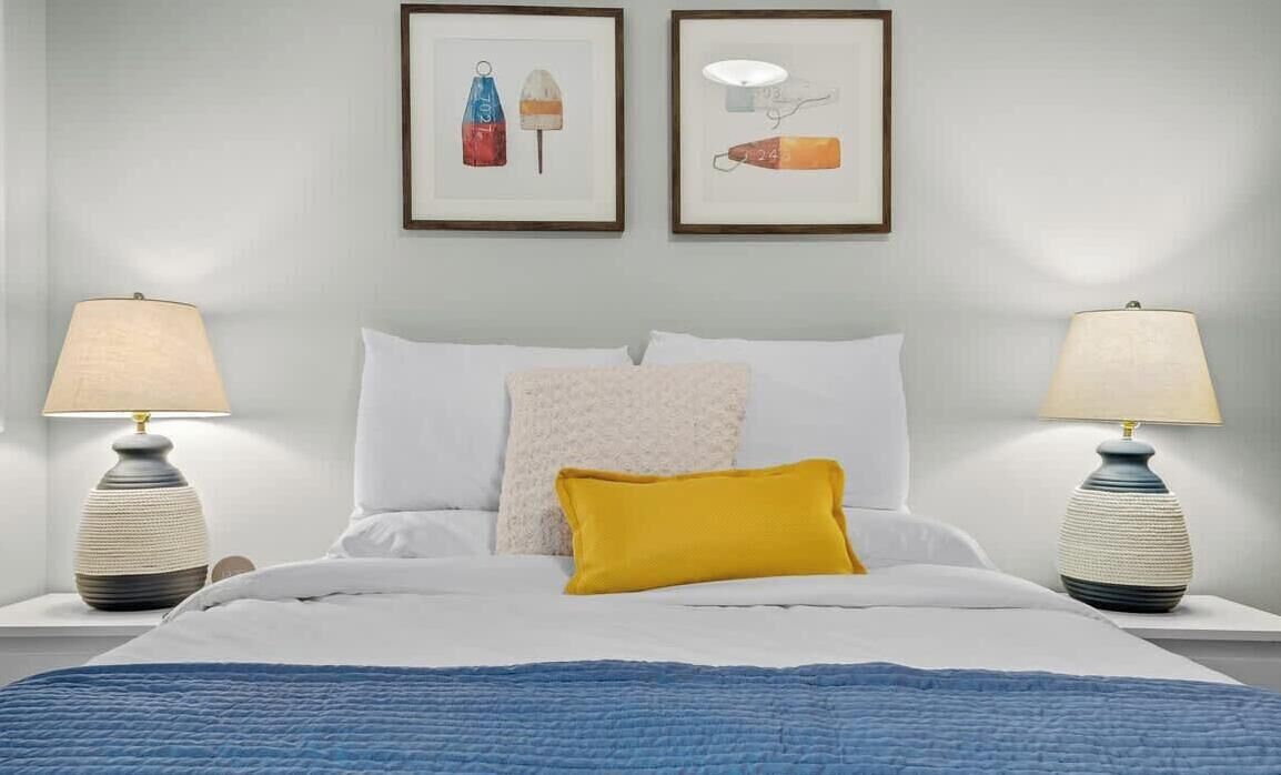 Un dormitorio con una cama, dos mesitas de noche, dos lámparas y dos cuadros en la pared.