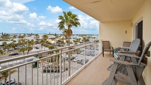 Un balcon donnant sur une rue, avec des palmiers et un immeuble en arrière-plan.