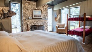 Un dormitorio con una cama grande, una pared de piedra, una chimenea, una cabeza de venado montada y una cama literera.
