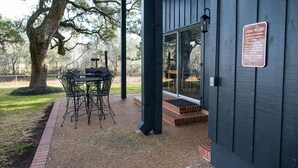 Un edificio de madera con una mesa y sillas afuera, un letrero con normas y un árbol grande cercano.