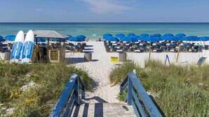 Ein Strand mit einer Holzpromenade, die zu einer Reihe blauer Sonnenschirme und Liegestühle führt.