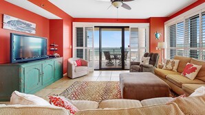 Sala de estar con televisor, sofá y sillones, ventilador de techo y balcón con vistas.